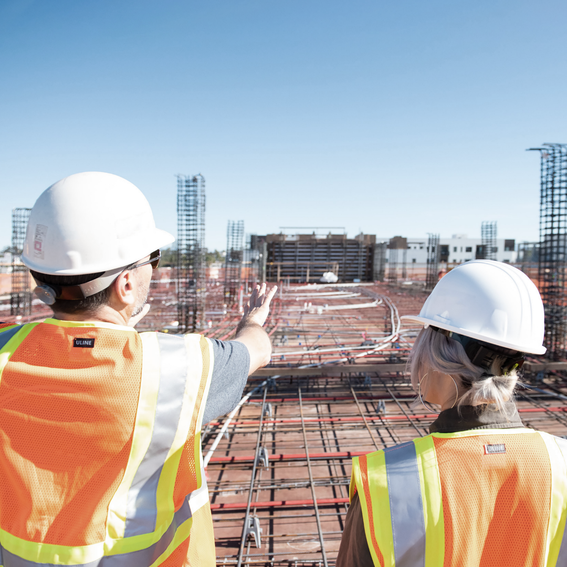 A man and a woman in hard hats and hi-vis jackets, overlooking a industrial site