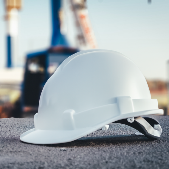 A white hard hat on black tarmac, a crane is blurred in the background