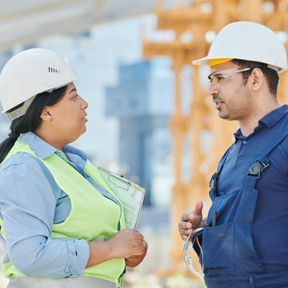 A man and a woman in white hard hats facing each other.