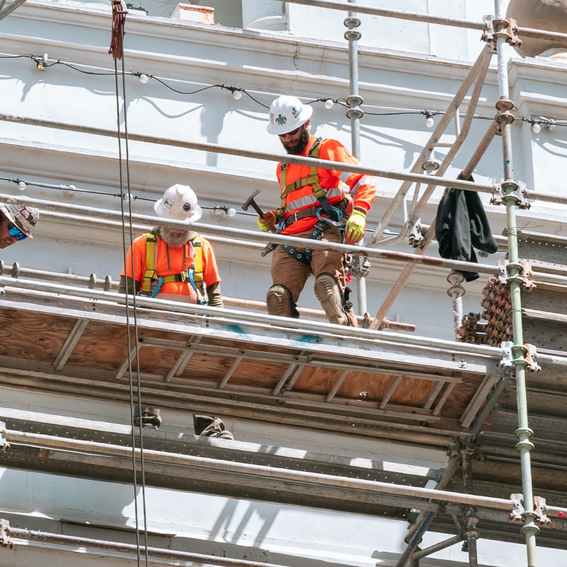 Two men on scaffolding in bright orange hi-vis jackets and white hard hats